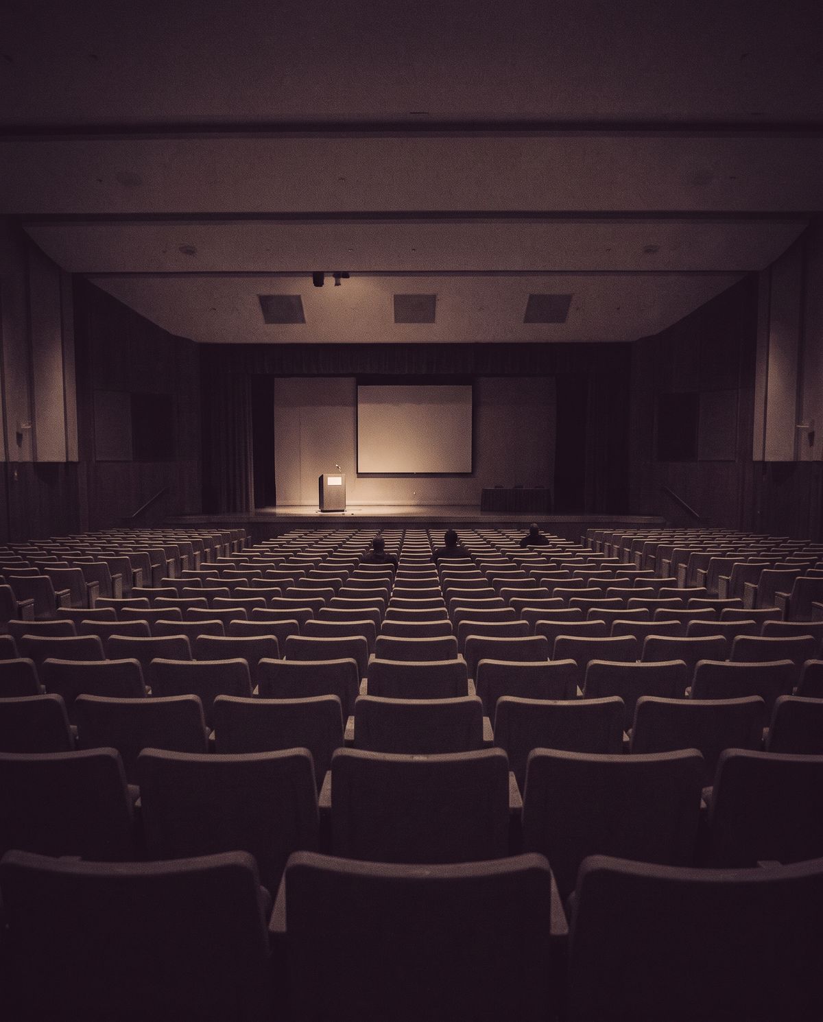 An almost empty conference auditorium with a single lit lectern on stage